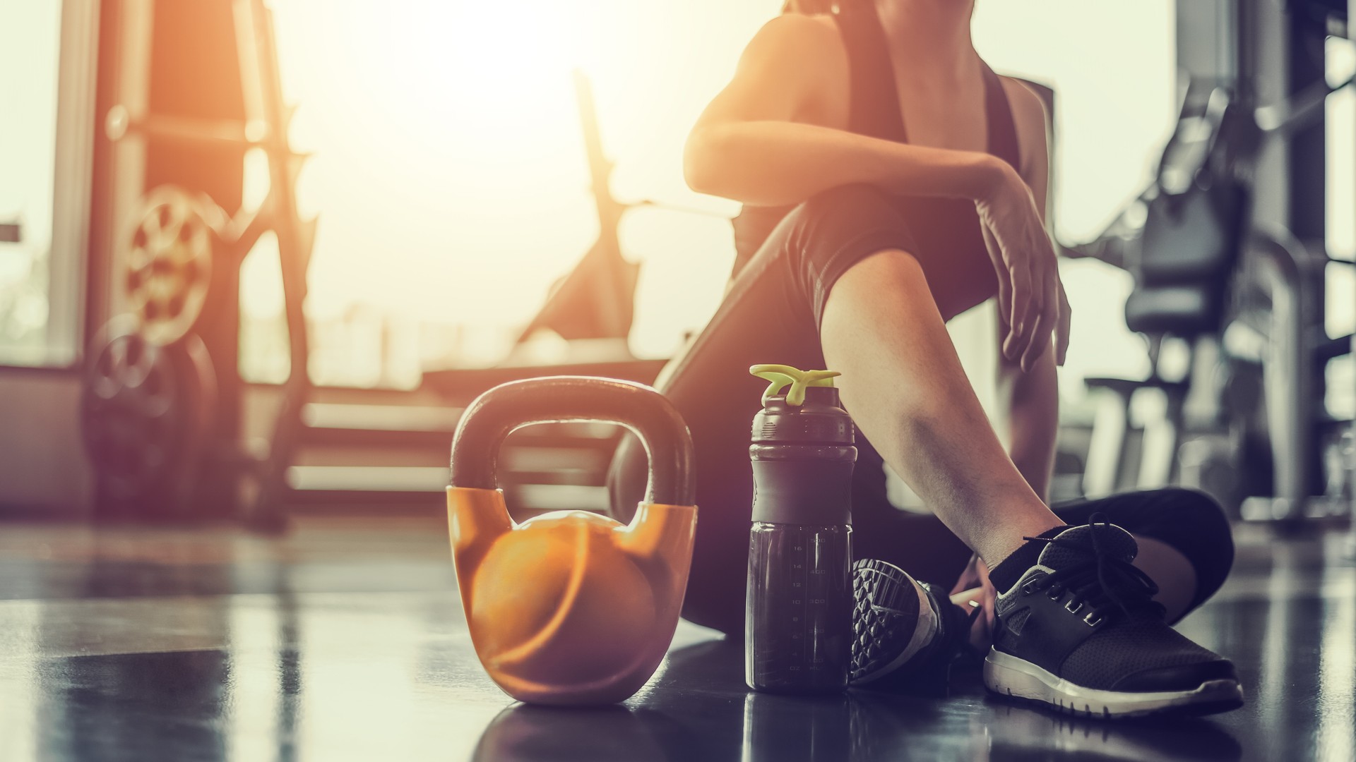 Young asian woman sitting taking a break relaxing after exercise with a whey protein and dumbbell placed beside at gym.